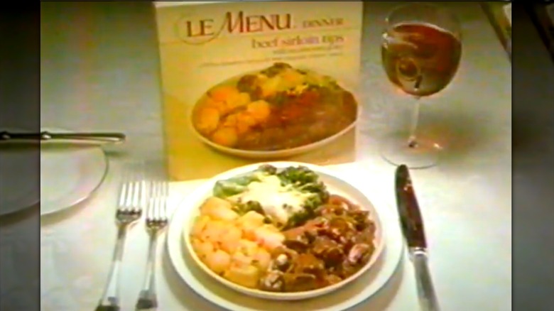 A plate of beef sirloin tips served in front of a Le Menu TV dinner box and glass of wine