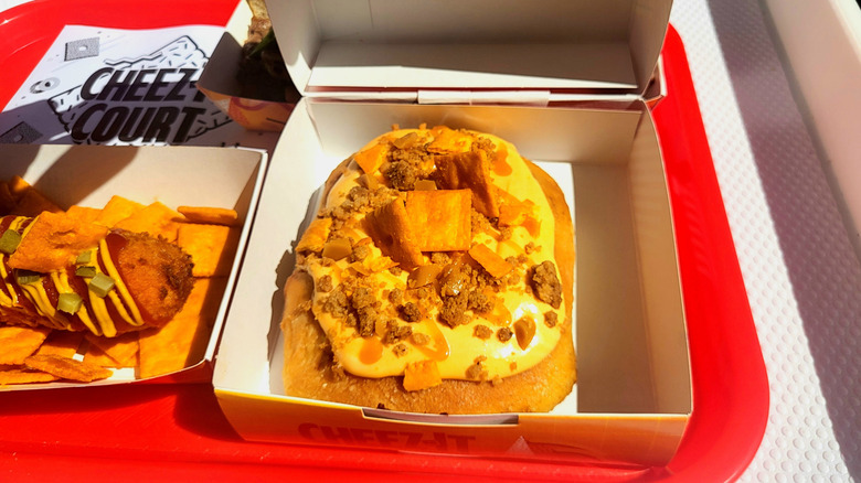 A cinnamon bun covered in yellow cheese frosting and sprinkled with Cheez-Its, crumbled shortbread, and salted caramel.