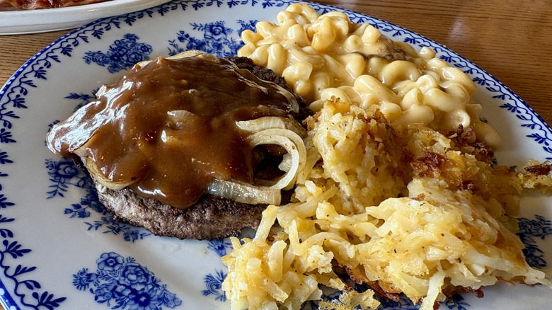 beef patty with brown gravy, mac and cheese, hashbrowns on decorative plate on table at Cracker Barrel