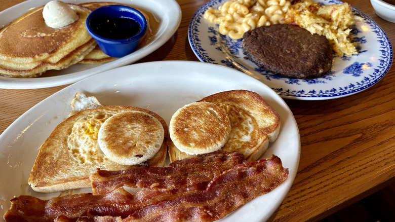 plate with toast, eggs, bacon in front of plate with beef and mac and cheese and another plate of pancakes on table at Cracker Barrel