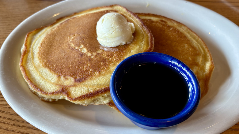 two pancakes with scoop of butter and blue cup of syrup on plate on table at Cracker Barrel