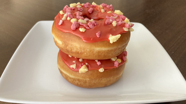 Two Dunkin' fruit punch donuts stacked on a white plate