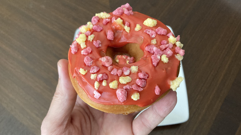 A hand holding a Dunkin' fruit punch donut