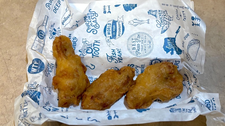 A closeup of Long John Silver's Crispy Battered Wings sitting on branded tissue paper on a neutral background