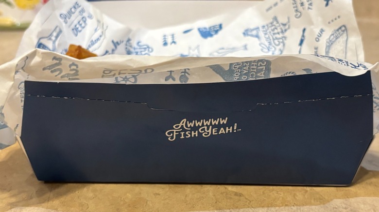 A closeup of a Long John Silver's branded food container with branded paper on a neutral background
