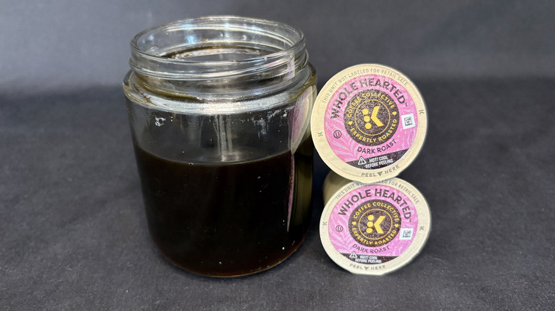 Dark coffee in a clear glass next to stacked K-Cups