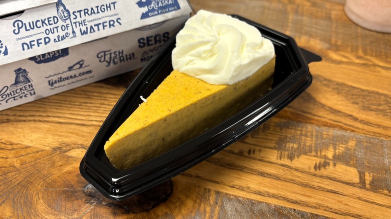 A piece of The Cheesecake Factory Bakery Pumpkin Cheesecake in black plastic container on wooden table
