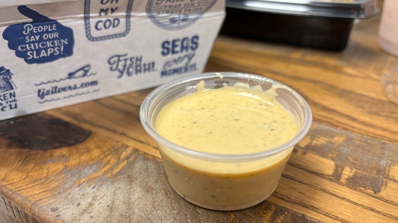 A close-up of Long John Silver's Ranch with Old bay in a plastic ramekin in front of branded box on wooden table