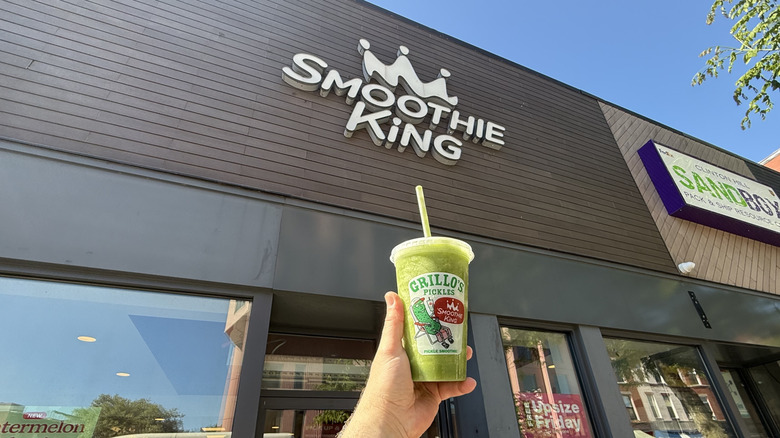 Hand holding a Smoothie King x Grillo's Pickles Smoothie in a plastic to-go cup outside of a Smoothie King