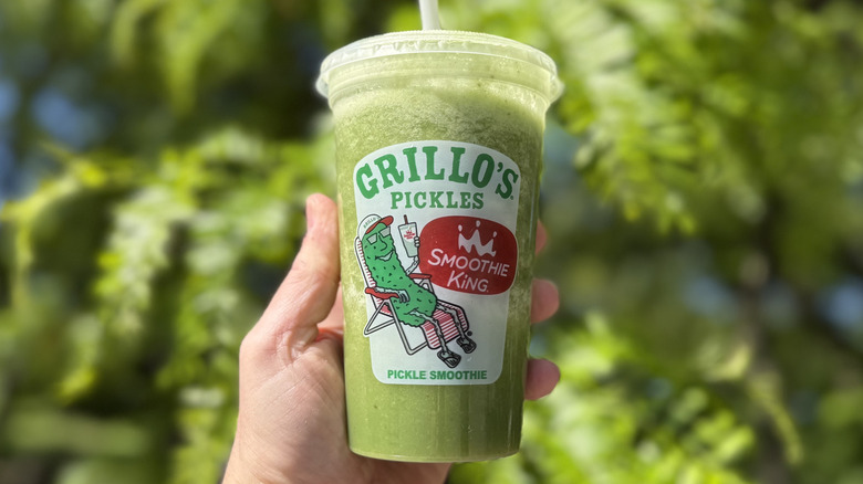 Hand holding a Smoothie King x Grillo's Pickles Smoothie in a plastic to-go cup raised in the air
