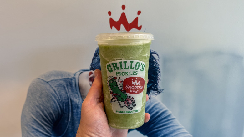 Hand holding a Smoothie King x Grillo's Pickles Smoothie in a plastic to-go cup below the Smoothie King logo