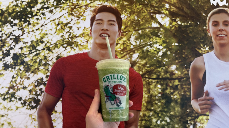 A photo of a jogger on a wall takes a sip of the Smoothie King x Grillo's Pickles Smoothie in the foreground