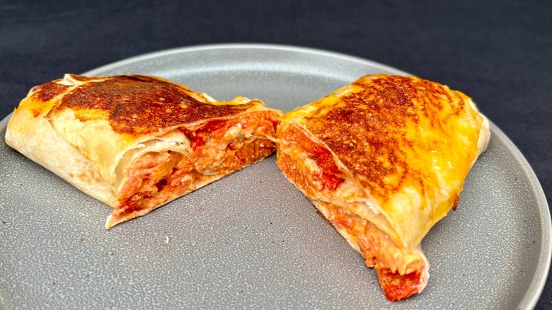 Taco Bell Grilled Cheese Burrito cut in half on plate with wrapped burrito behind it