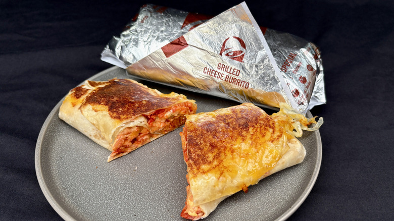 Taco Bell Grilled Cheese Burrito cut in half on plate with wrapped burrito behind it