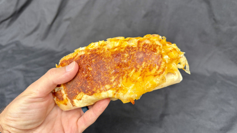 hand holding cheese covered burrito with black background