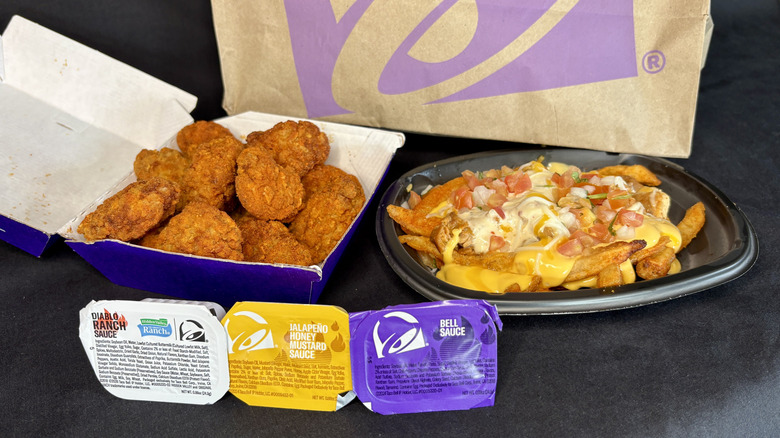 Taco Bell chicken nuggets, nacho fries, three dipping sauces with bag in background
