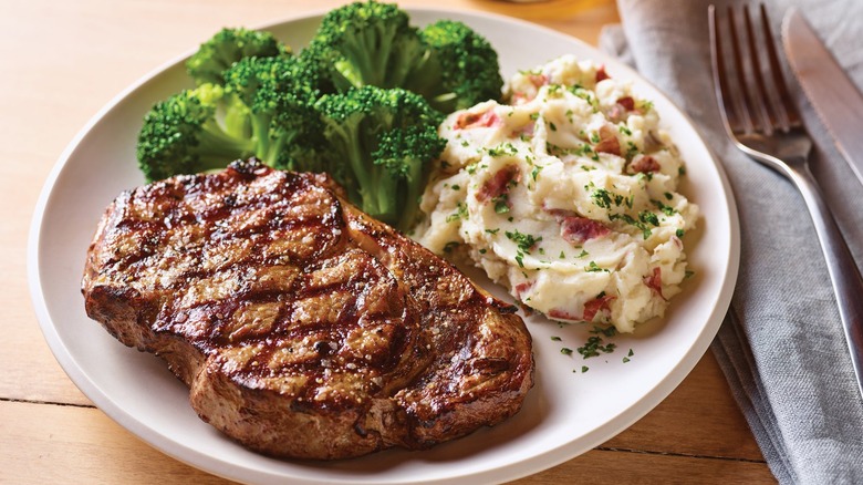 Ribeye with broccoli and smashed potatoes on a white plate