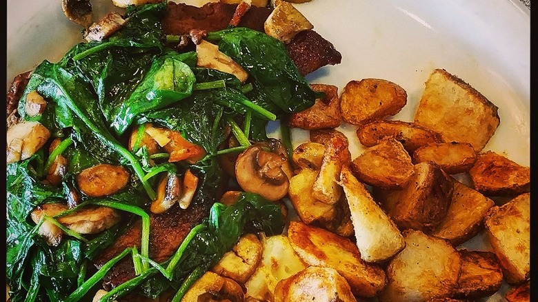 Sirloin steak smothered in spinach with potatoes on a white plate