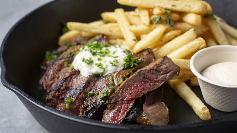 Sliced steak with herbed butter and fries in a cast iron pan