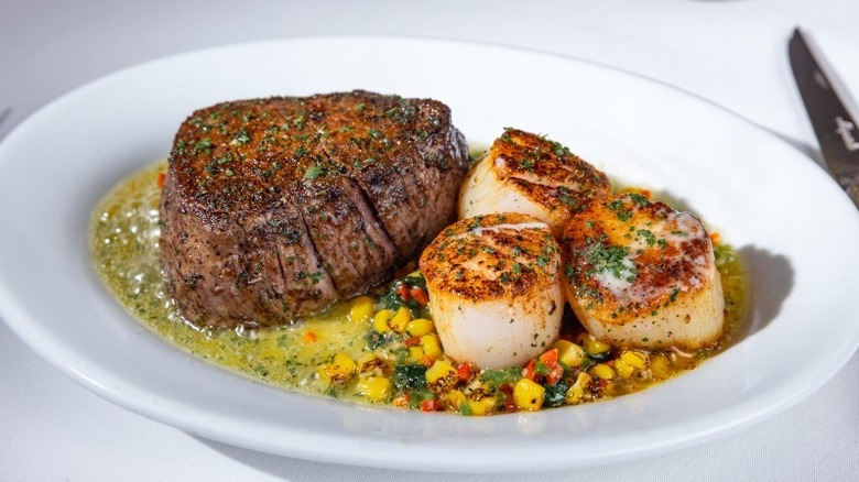 Filet mignon and sea scallops on bed of corn on a white plate
