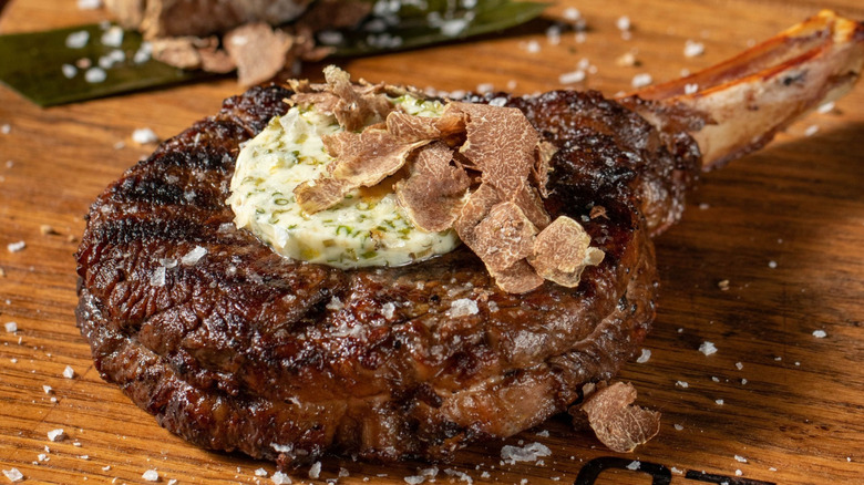 Ribeye steak with herbed butter, shaved truffles, and flaky sea salt on a wooden cutting board