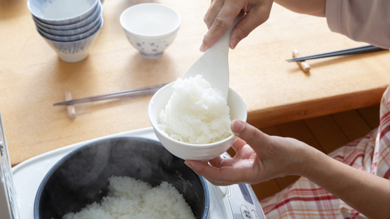A hand taking white rice out of a rice cooker and placing it in a bowl.