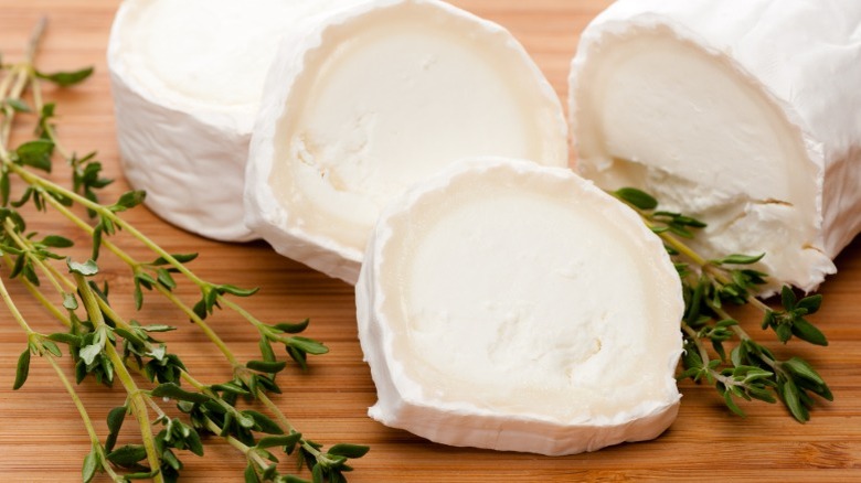 Sliced log of goat cheese on a cutting board with thyme