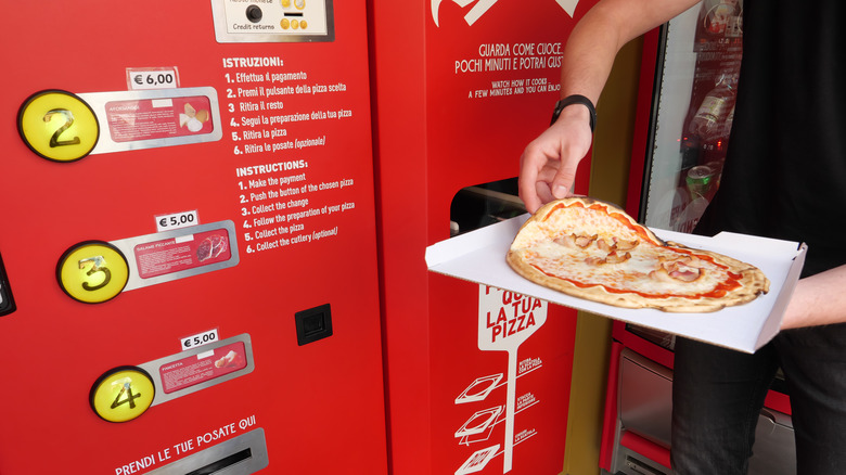 A person pulling a pizza out of a vending machine