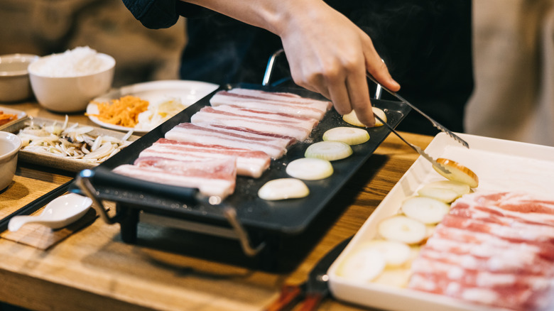 A server helping cook food at a Korean barbecue restaurant