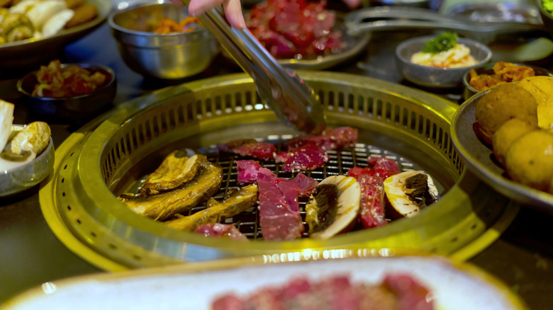 Hands holding tongs on a Korean bbq grill