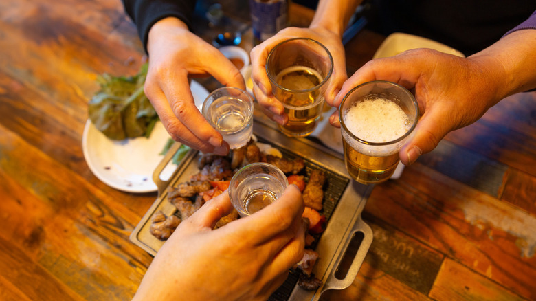 Hands clinking glasses over a Korean bbq grill