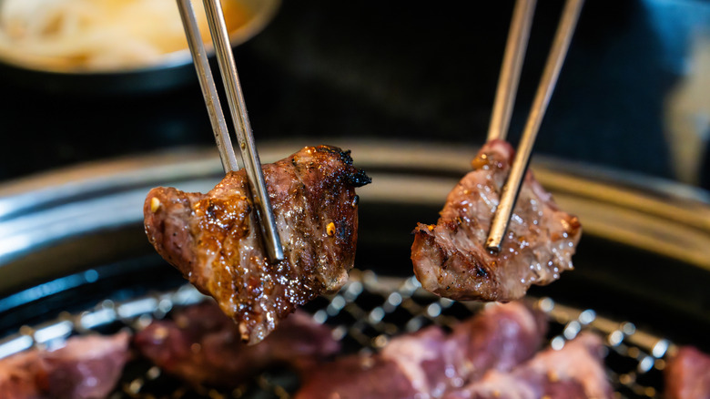 Metal chopsticks with pieces of meat over a grill