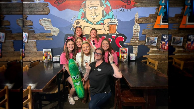 A group of ladies posing with a Dick's Last Resort waitress holding up two middle fingers