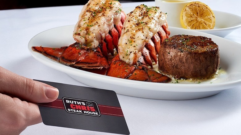 A person holding a Ruth's Chris gift card in front of a plate of steak and lobster