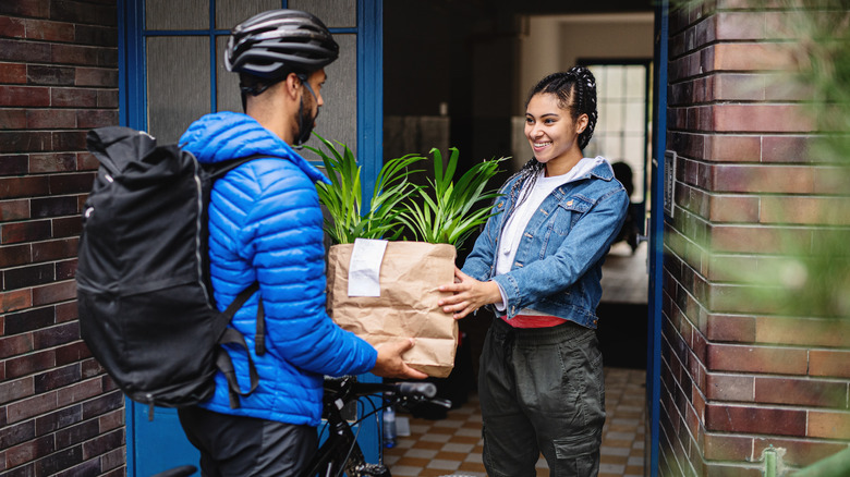 A bicyclist delivering food in a paper bag to a smiling woman
