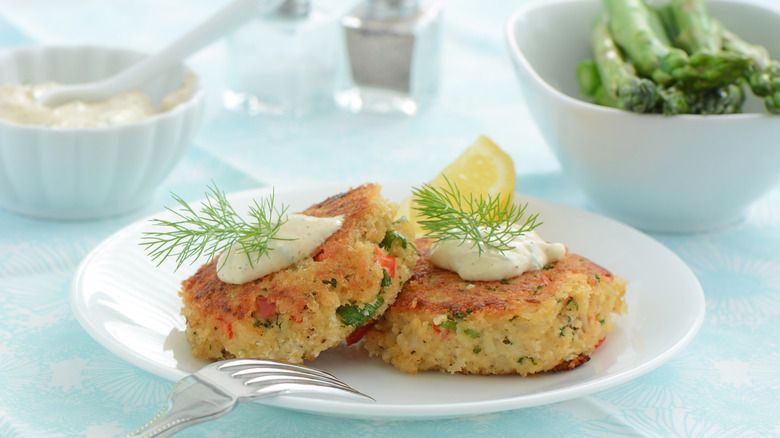 A plate of crab cakes garnished with sauce, dill, and lemon slice