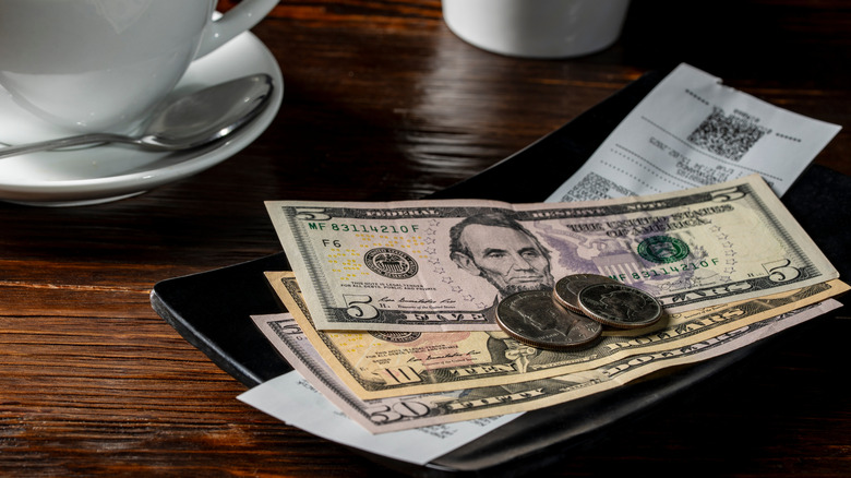 Cash and coins on top of a restaurant bill next to a cup and spoon