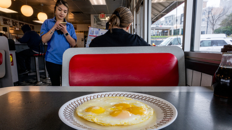 A plate of sunny-side up eggs on a Waffle House table with an employee taking an order in the background