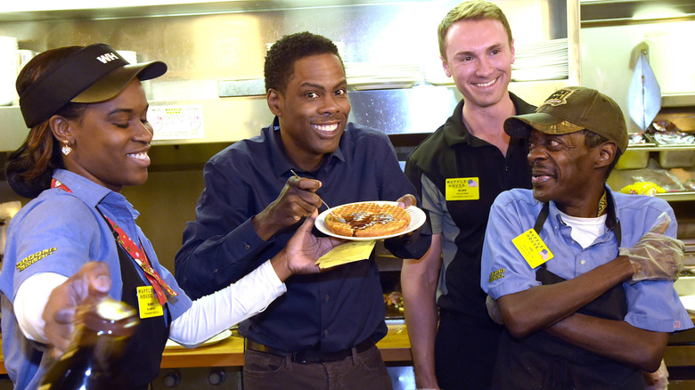 Waffle House employees posing with Chris Rock holding a plate with a waffle