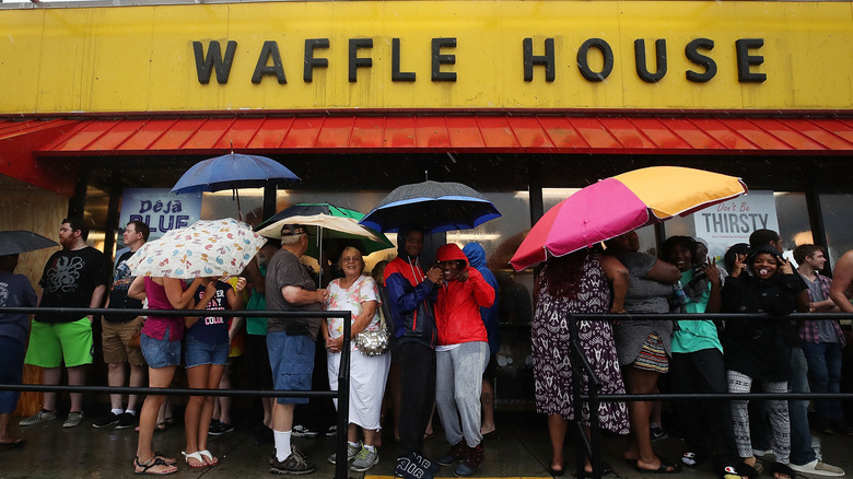 A large group of customers holding umbrellas in front of Waffle House