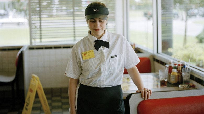 A Waffle House employee smiling shyly while resting hand on booth