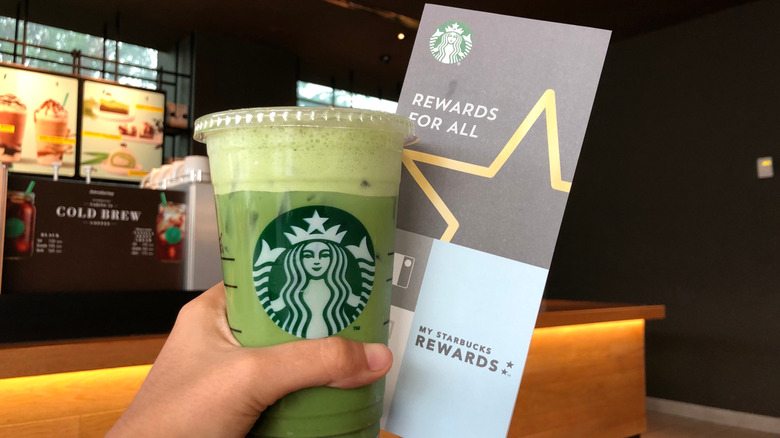 Hand holds Starbucks drink and rewards sign