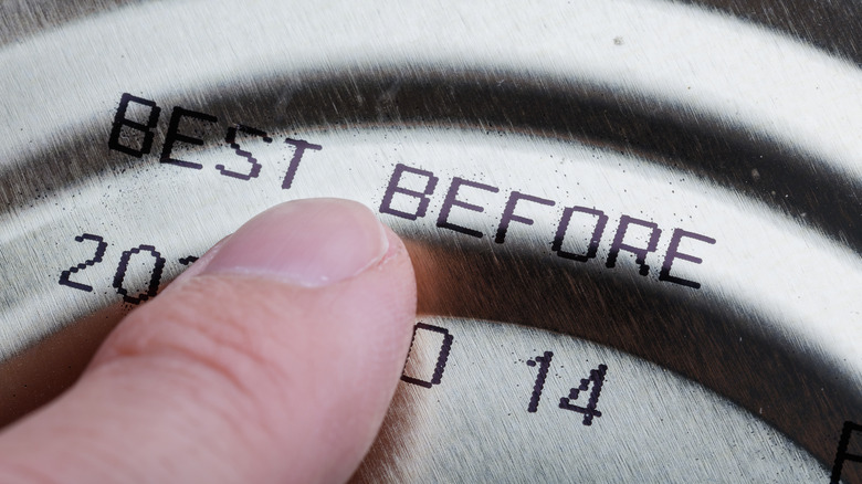 A closeup of a finger pointing at a "best before" date of a canned food