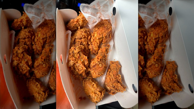 A man holds up a box of Popeyes ghost pepper wings to the camera