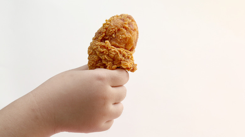 A hand of a child holding a fried chicken drumstick