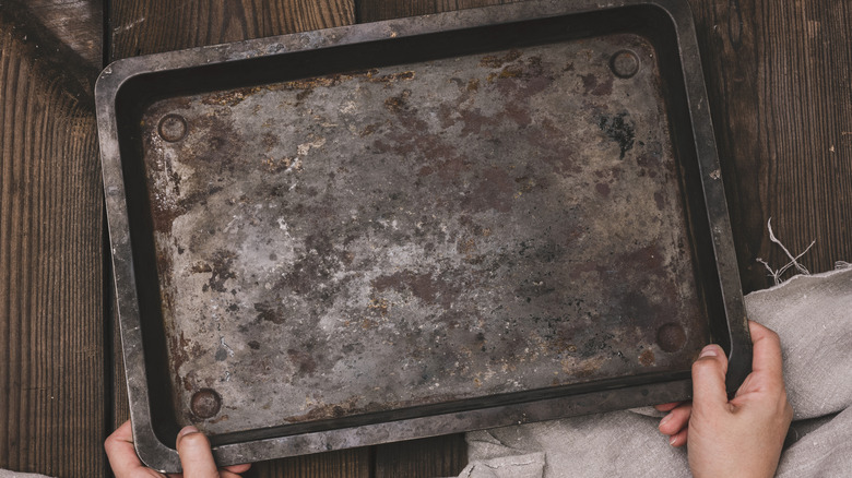 Hands holding rusty baking sheet