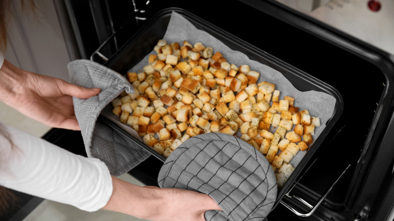 Hands removing homemade croutons from oven