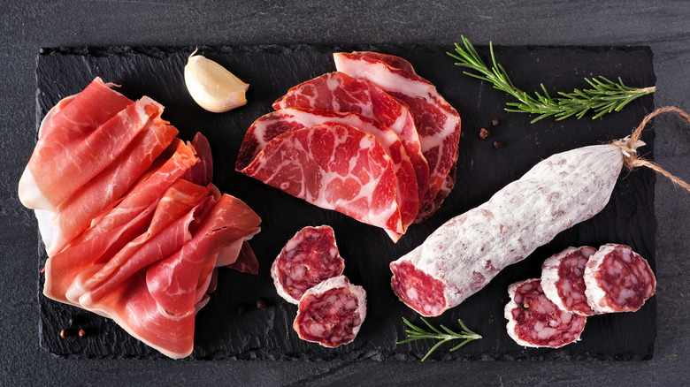 Italian cold cuts and salami on a black cutting board with garlic and spices