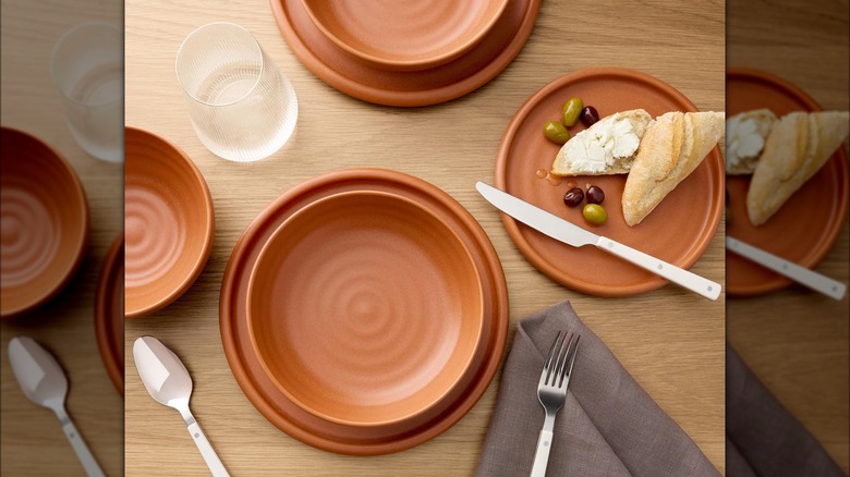 A set of orange dinner plates from Sam's Club on wood table with utensils.