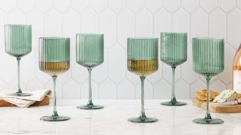 A set of ribbed wine glasses on marbled counter with cheese plate in background.